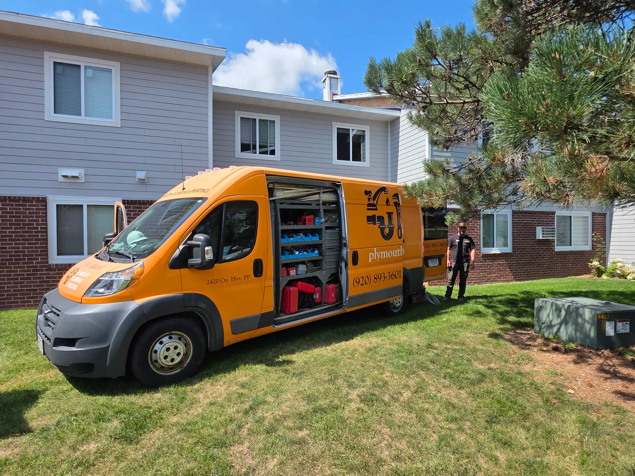 Plymouth Plumbing & Heating service van on a job, side door open to stocked parts shelves, with one of the crew alongside